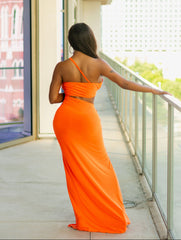 Woman in an orange dress standing on a balcony with a cityscape view.