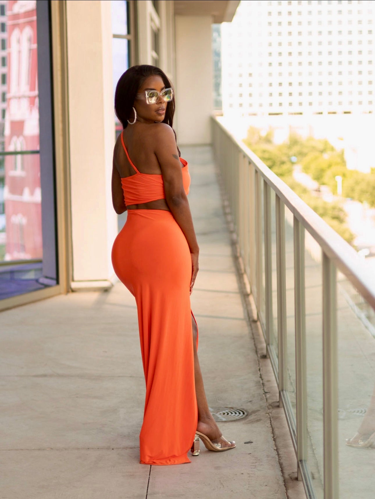 Woman in an orange dress standing on a balcony with a cityscape background