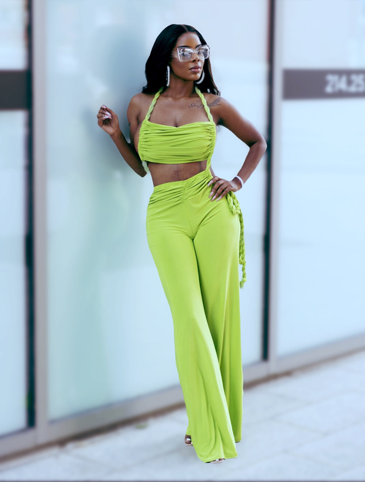 Woman wearing a bright green outfit standing against a glass wall.