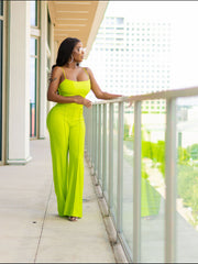 Woman in a bright green jumpsuit standing on a balcony with a cityscape view.
