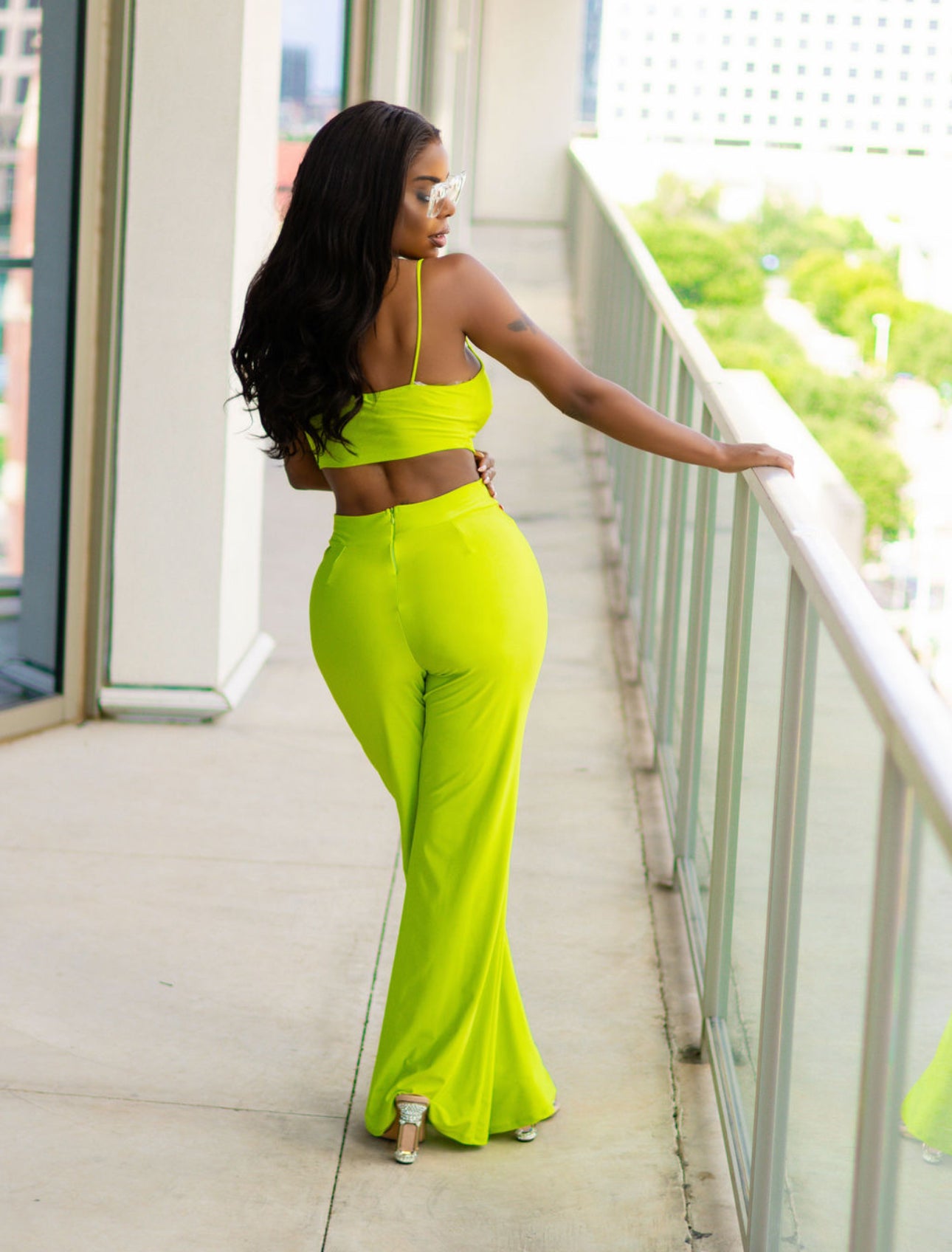 Woman in a bright green outfit standing on a balcony with a cityscape background