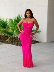 Woman wearing a bright pink strapless gown standing outdoors with greenery in the background